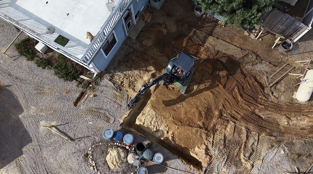 Aerial drone view of mini-excavator digging foundation trench
